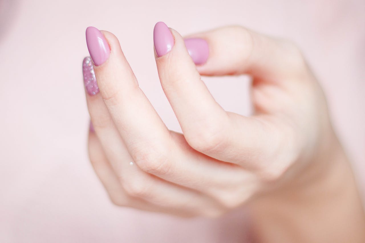 A close-up of a womans hand showing a stylish pink and glittery manicure.